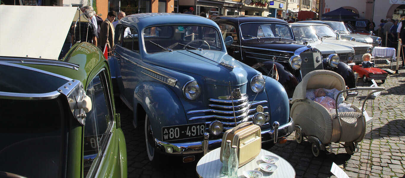 Mehrere Oldtimer, alter Puppenwagen und altes Radio auf dem Bad Mergentheimer Marktplatz.